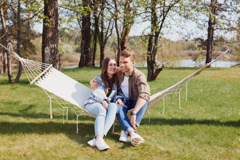 Happy young man hugging her girlfriend while sitting on hammock together scaled